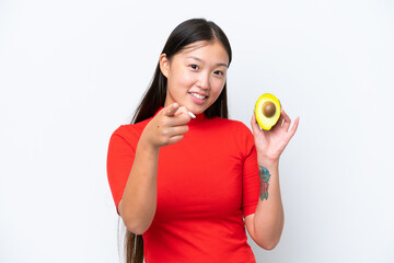 Young Asian woman holding an avocado isolated on white background points finger at you with a confident expression