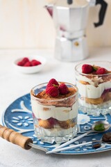 Dessert, tiramisu with raspberries in portioned glass glasses on a blue metal tray on a light concrete background. Italian Cuisine. Valentine's day