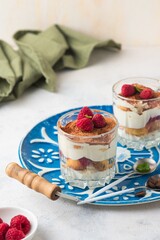 Dessert, tiramisu with raspberries in portioned glass glasses on a blue metal tray on a light concrete background. Italian Cuisine. Valentine's day