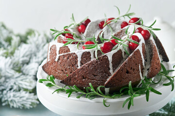 Christmas chocolate bundt cake. Traditional Christmas fruit cake with white glaze, cranberries and rosemary on white stand with Christmas decoration. Winter baking at Xmas or New Year. Copy space.