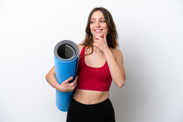 Young sport caucasian woman going to yoga classes while holding a mat isolated on white background looking to the side and smiling