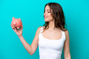 Young Caucasian woman holding a piggybank isolated on blue bakcground with happy expression