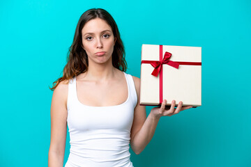 Young caucasian woman holding a gift isolated on blue background with sad expression