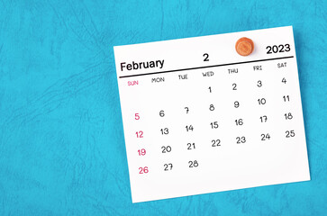 The February 2023 monthly calendar and wooden push pin on blue background.