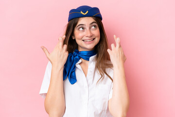 Airplane stewardess caucasian woman isolated on pink background with fingers crossing