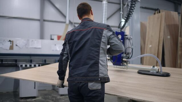 worker use vacuum lifter to relocate wooden or chipboard workpiece in workshop of plant