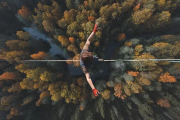 Foto op Plexiglas Highline over the forest. Rope walker walks on a rope at high altitude. Drone view. Slackline theme © Happyphotons
