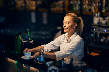 Bartender is serving cup of fresh coffee while standing at a bar.