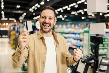 A happy man showing credit card at the camera and smiling at supermarket.