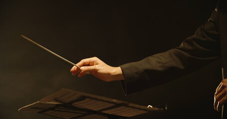 Close up shot of hands of symphony orchestra conductor directing music by waving his baton. Studio...