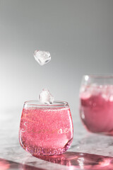 The glasses og pink drink and ice falling into glass