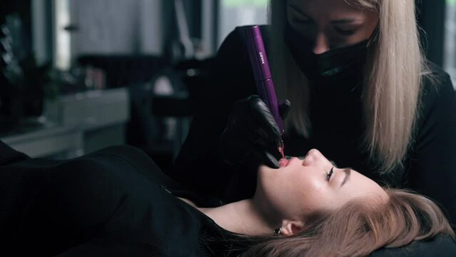 Permanent lip makeup. The cosmetologist makes the procedure of permanent makeup to the client in the salon.