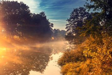 Wschód słońca. Jesienny poranek nad dziką rzeką w Polsce. Odbicia w wodzie. Wodny krajobraz. Świt. Kolory jesieni. Jesienne scenerie. Mgliste poranki. Bez ludzi. Tło natury.