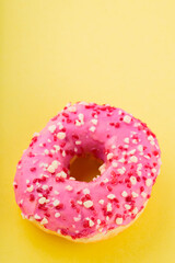 Strawberry donut with pink icing and sprinkles. Sweet pink donut on yellow background. Flat lay. Copy space