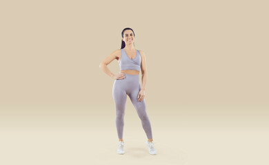 Obraz na płótnie Canvas Fit and healthy woman. Portrait of happy sportswoman dressed in comfortable sportswear set isolated on beige background. Full length of smiling young woman with athletic body in light lilac sportswear