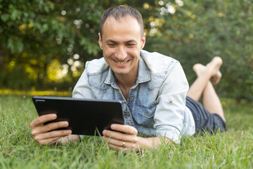 young man student freelancer using digital tablet reading e-book, working remotely, surfing on Internet, social media, checking e-mails, e-learning, e-banking online in city