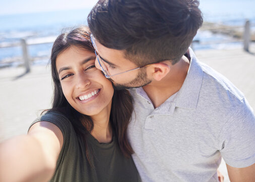 Couple, love and selfie at the beach, travel and kiss by ocean with support, trust and care with adventure in Mumbai. Smile in picture, happy and memory with smartphone photography for romance