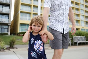 little girl holding dads hand on boardwalk in summer smiling