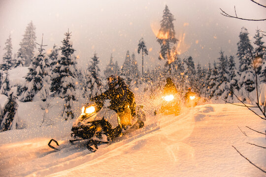 People driving snowmobiles at sunset, Callaghan Valley, Whistler, British Columbia, Canada