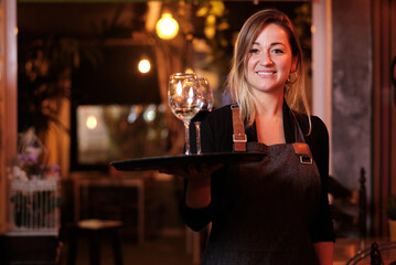 Waitress looking at the camera and smiling while holding a tray with wine glasses.