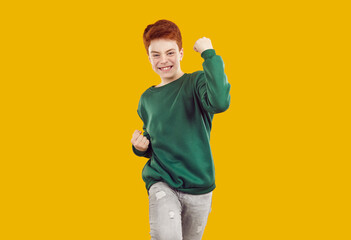 Joyful child celebrating success. Overjoyed preteen boy with happy face expression standing isolated on orange background, clenching fists, doing yes gesture and smiling
