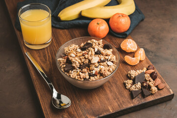 Granola cereal oatmeal with chocolate, banana and nuts in a bowl on dark wooden board