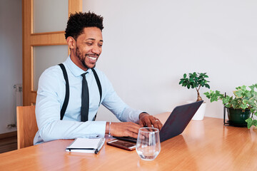 Businessman smiling while working with laptop sitting on a desk indoors.