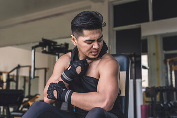 An asian man feel a sudden jolt of pain in his shoulder. a torn or sprained rotator cuff at the gym.