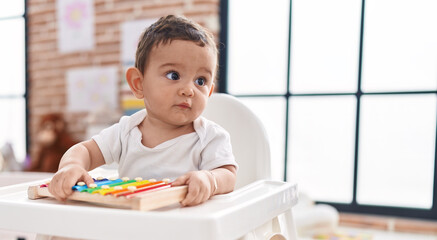 Adorable hispanic baby sitting on highchair playing xylophone at kindergarten