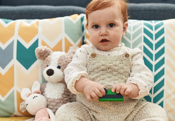 Adorable redhead toddler playing with car toy sitting on sofa at home