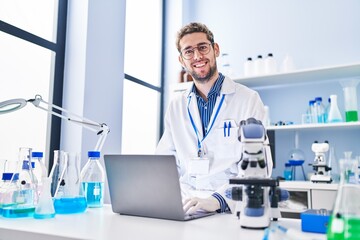 Young man scientist smiling confident using laptop at laboratory