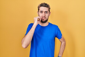 Hispanic man with beard standing over yellow background mouth and lips shut as zip with fingers....