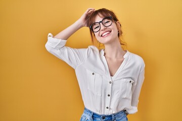 Young beautiful woman wearing casual shirt over yellow background smiling confident touching hair...
