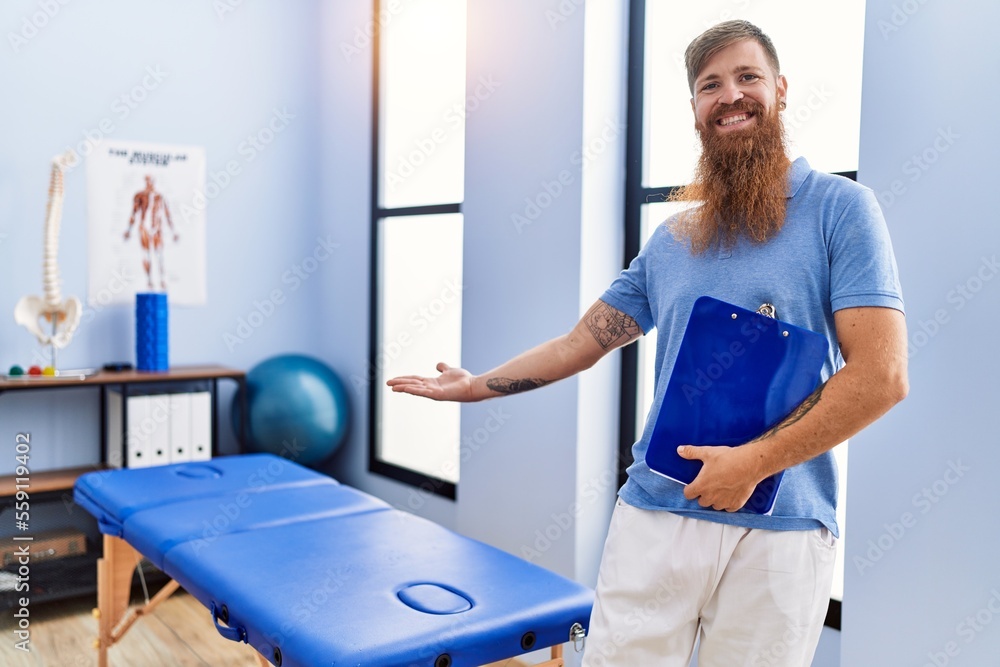 Poster young redhead man wearing physiotherapist uniform holding clipboard at physiotherapy clinic