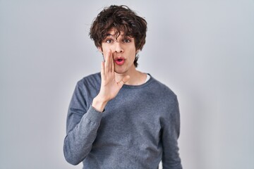 Young man standing over isolated background hand on mouth telling secret rumor, whispering malicious talk conversation