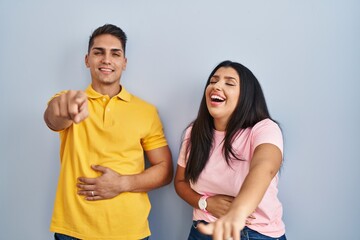 Young couple standing over isolated background laughing at you, pointing finger to the camera with hand over body, shame expression