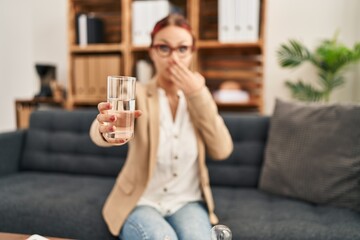 Young caucasian woman offering a glass of water covering mouth with hand, shocked and afraid for...