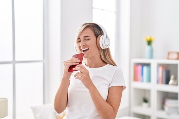 Young blonde woman listening to music singing song at bedroom