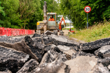 Excavator with hydraulic jack hammer  breaking asphalt in preparation for drainage works close up and selective focus