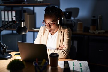 Beautiful black woman working at the office at night afraid and shocked with surprise expression, fear and excited face.