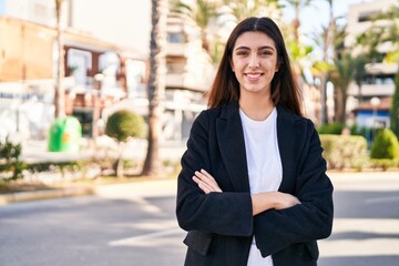 Young beautiful hispanic woman standing with arms crossed gesture at street