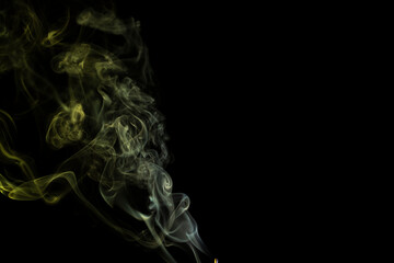 incense stick with yellow green  smoke against black background