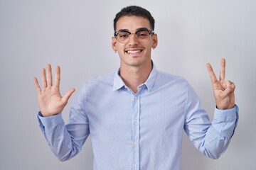 Handsome hispanic man wearing business clothes and glasses showing and pointing up with fingers number seven while smiling confident and happy.