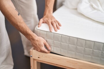 Young hispanic man holding mattress at bedroom