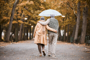 Elderly, couple walk in park with umbrella and fresh air, outdoor in nature in fall for exercise and retirement together. Hug, love and care with trees, senior man and woman in New York back view.