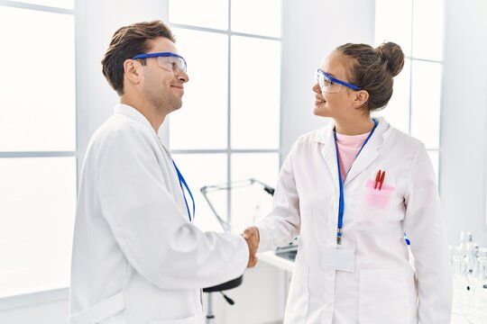 Man and woman wearing scientist uniform shake hands at laboratory
