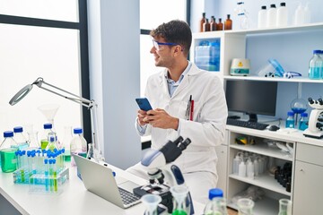 Young hispanic man scientist smiling confident using smartphone at laboratory