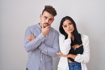 Young hispanic couple standing over white background thinking looking tired and bored with depression problems with crossed arms.
