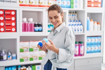 Young woman customer smiling confident holding deodorant bottles at pharmacy