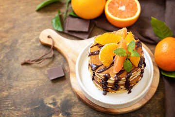 Celebrating Pancake day, healthy american breakfast. Delicious bananas pancakes with chocolate and red oranges on rustic table.